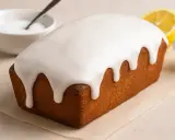 Un délicieux cake au citron recouvert d'un glaçage sucre glace facile, avec une tranche de citron et un bol d'ingrédients à proximité.