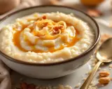 Un bol de riz au lait crémeux, nappé de caramel et garni de copeaux dorés. Une cuillère dorée repose à côté.