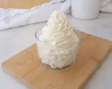 Crème au beurre sucre glace, onctueuse et aérienne, dressée dans un verre sur une planche en bois.