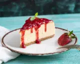 Tranche de cheesecake à la ricotta sans cuisson, nappée de coulis de fraises et décorée d'une feuille de menthe. Une fraise entière et une fourchette complètent la présentation.
