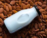 Bouteille de lait d'amande maison posée sur un lit d'amandes entières.