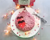 Gâteau rose orné de cœurs, enrobé de chocolat ruby croquant. Guirlande lumineuse et confettis ajoutent une touche festive.