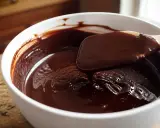 Une spatule mélange une ganache au chocolat brillante dans un bol blanc. Une astuce pour comment rattraper une ganache trop liquide est de la laisser refroidir.