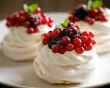 Trois mini pavlovas garnis de crème fouettée et de fruits rouges frais, dont des groseilles et des mûres.