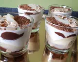 Quatre verrines poire chocolat mascarpone, garnies de copeaux de chocolat et d'amandes effilées, sur un plateau doré.