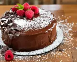 Un délicieux cake au chocolat, nappé de glaçage brillant, décoré de framboises fraîches, de copeaux de chocolat et saupoudré de sucre glace.