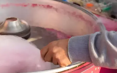 Main d'une personne récoltant du sucre filé rose, étape clé pour savoir comment faire du sucre à barbe à papa.