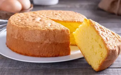 Un moelleux gâteau de Savoie, parfait pour la conservation, avec une part coupée. Des œufs et un fouet en arrière-plan suggèrent sa préparation.