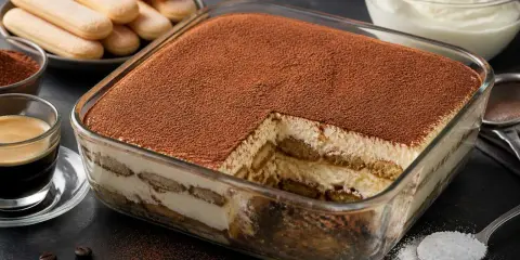 Un délicieux tiramisu caramel, généreusement saupoudré de cacao, prêt à être dégusté. Des biscuits à la cuillère et une tasse d'espresso complètent cette gourmandise.