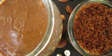 Deux pots de praliné maison, l'un crémeux, l'autre concassé, entourés d'amandes et de noisettes. La conservation est assurée !