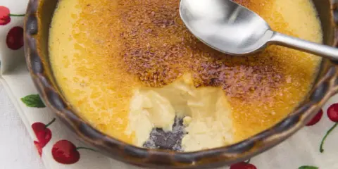 Crème brûlée avec une croûte caramélisée craquante. Une cuillère est posée sur le dessert, parfait pour une recette de crème brûlée facile et rapide.