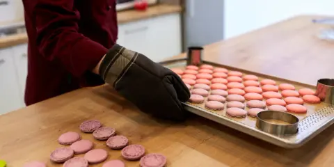 Préparation pour la cuisson macaron four traditionnel : une plaque de macarons roses et roses est prête, des cercles à pâtisserie sont à proximité.