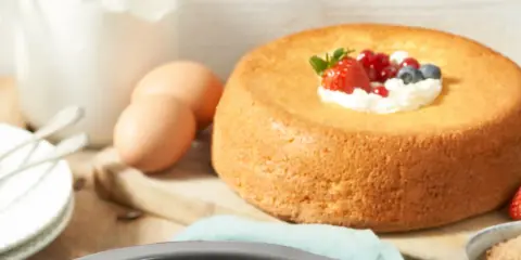 Un savarin traditionnel, doré et moelleux, garni de crème fouettée et de fruits rouges. Des œufs et de la farine sont prêts pour la préparation.