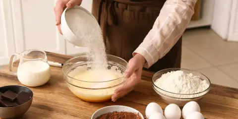 Préparation d'un gâteau : on verse du sucre dans un bol, une alternative pour remplacer le sucre blanc. Ingrédients : œufs, lait, farine, cacao, chocolat.