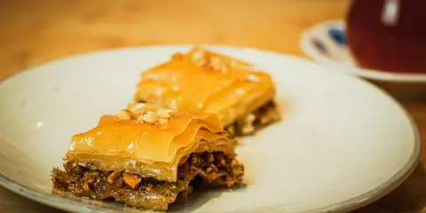 Deux parts de baklava, garnies de noix, sur une assiette. Une recette de baklava qui fait saliver.