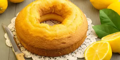 Gâteau moelleux au mascarpone et citron, prêt à être dégusté. Des citrons frais et une touche de verdure complètent la scène.