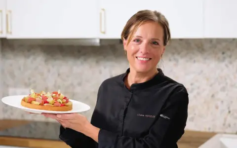 Pâtissière souriante tenant une tartelette aux fruits, peut-être préparée avec de la pectine ou de la gélatine pour une texture parfaite.
