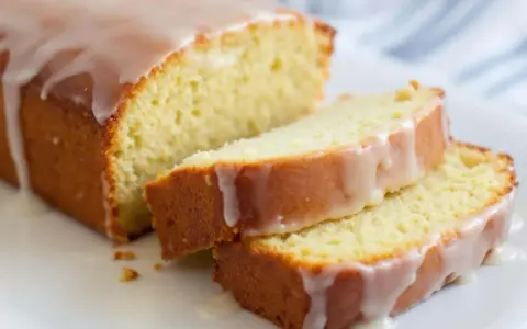 Un délicieux gâteau courgette citron, nappé d'un glaçage blanc, est coupé en tranches sur une assiette blanche.