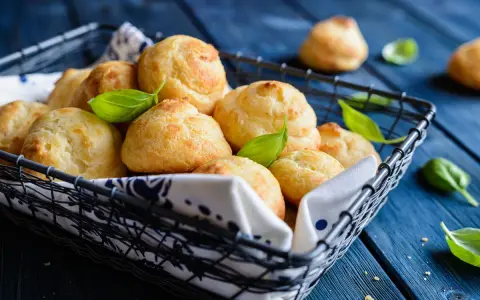 Gougères dorées dans un panier, garnies de feuilles de basilic. Si les vôtres ne gonflent pas, vérifiez la température du four !