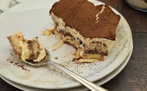 Une part de tiramisu nutella, saupoudrée de cacao, sur une assiette. Une cuillère en argent a prélevé un morceau crémeux.