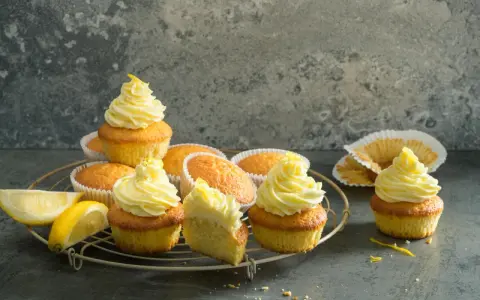 Plusieurs cupcakes citron avec un glaçage jaune vif, certains décorés de zestes. Des quartiers de citron frais sont posés à côté.