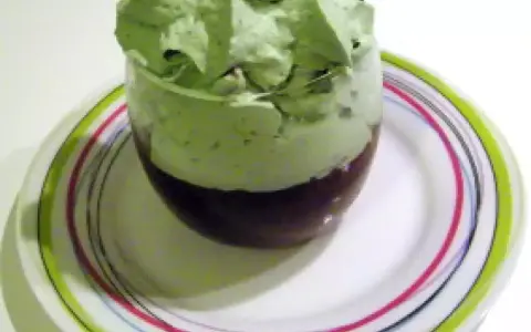 Un verre de dessert avec une couche de chocolat au fond et une généreuse chantilly pistache aérienne sur le dessus, posé sur une assiette colorée.