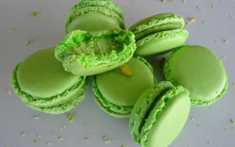 Macarons verts vifs, certains ouverts révélant une garniture crémeuse. Parfaits pour une recette ganache pistache sans chocolat blanc.