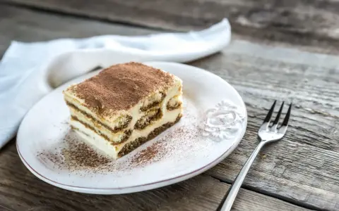 Une part de tiramisu sur une assiette blanche, saupoudrée de cacao. Combien de temps au frigo pour ce délice ?