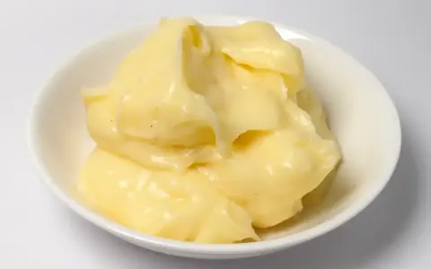 Crème pâtissière onctueuse, légèrement granuleuse, dans un bol blanc. Des points noirs de vanille parsèment la texture crémeuse.