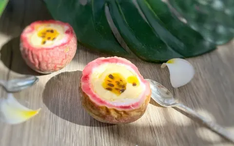 Deux moitiés de fruit de la passion garnies d'une crème jaune et de graines noires, sur une table en bois, avec une feuille tropicale et des pétales de fleurs.