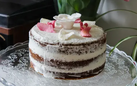 Un délicieux layer cake fleuri, avec des pétales de roses en sucre roses et blancs, posé sur un plat en verre orné.