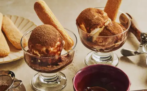 Deux coupes de glace tiramisu, saupoudrées de cacao, avec des biscuits à la cuillère. Un délice glacé à savourer.