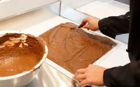 Un chef étale une pâte chocolatée onctueuse dans un moule. C'est la base du praliné, une gourmandise qui fait rêver.