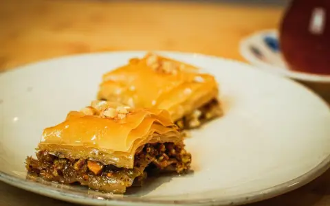 Deux parts de baklava, garnies de noix, sur une assiette. Une recette de baklava qui fait saliver.