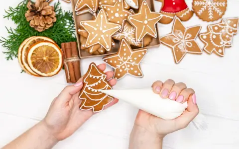 Mains décorant un biscuit sapin avec du glaçage royal. Autour, des étoiles et des décorations de Noël.
