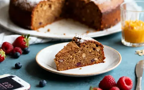 Tranche de gâteau aux noix et fruits rouges, saupoudrée de sucre glace. Une option saine pour un dessert, peut-être préparée avec de la **stevia pour gâteau**.
