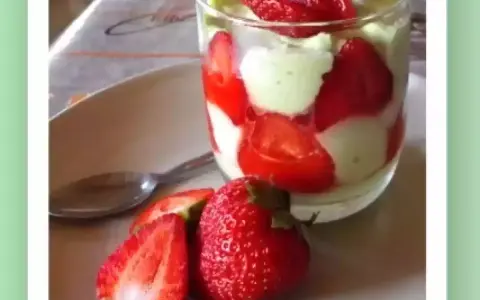 Un délicieux tiramisu pistache fraise, présenté en verrine avec des fraises fraîches sur le côté.