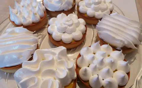 Plusieurs tartelettes garnies de crème citronnée et couronnées de meringue italienne aux formes variées.