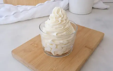 Crème au beurre sucre glace, onctueuse et aérienne, dressée dans un verre sur une planche en bois.