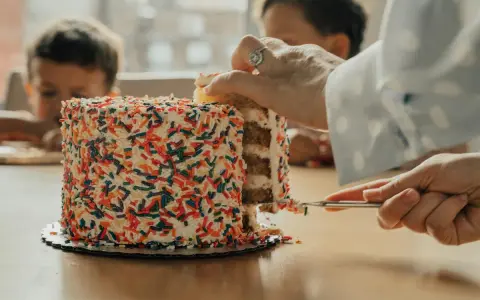Une main coupe une part d'un gâteau coloré de vermicelles. Apprenez comment couper un layer cake pour un partage parfait.