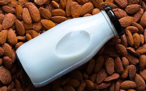 Bouteille de lait d'amande maison posée sur un lit d'amandes entières.