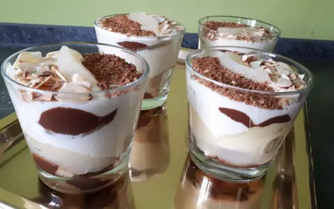 Quatre verrines poire chocolat mascarpone, garnies de copeaux de chocolat et d'amandes effilées, sur un plateau doré.