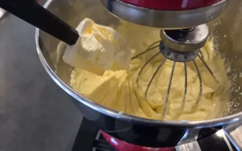 Une spatule ajoute une touche finale à une crème mousseline légère dans un robot pâtissier.