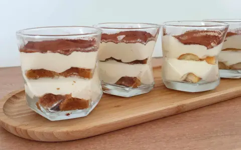Quatre verrines de tiramisu chantilly mascarpone, superposant biscuits imbibés et crème onctueuse, saupoudrées de cacao.