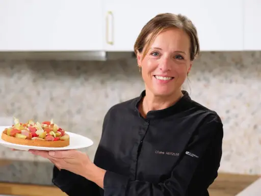 Pâtissière souriante tenant une tartelette aux fruits, peut-être préparée avec de la pectine ou de la gélatine pour une texture parfaite.