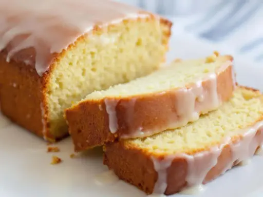 Un délicieux gâteau courgette citron, nappé d'un glaçage blanc, est coupé en tranches sur une assiette blanche.