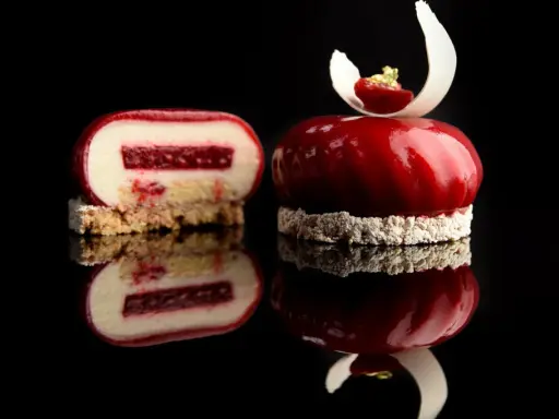 Un entremet rouge vif, miroir de la gourmandise. Une coupe révèle sa texture délicate, parfaite pour une recette entremet.