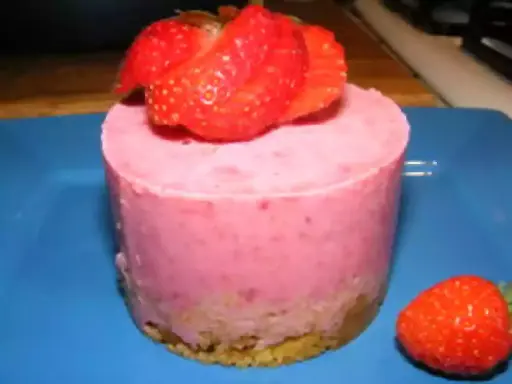 Gâteau individuel rose vif, garni de fraises fraîches. Un délice au glacage fraise sur fond bleu.