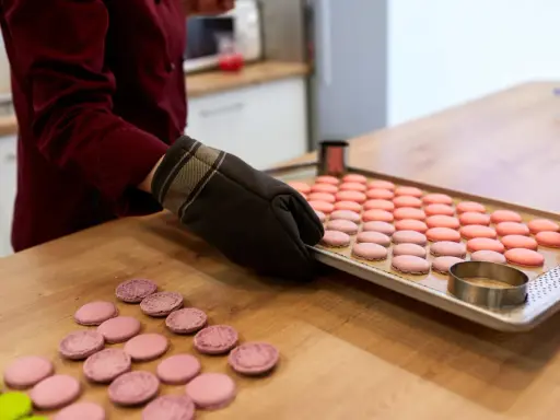 Préparation pour la cuisson macaron four traditionnel : une plaque de macarons roses et roses est prête, des cercles à pâtisserie sont à proximité.