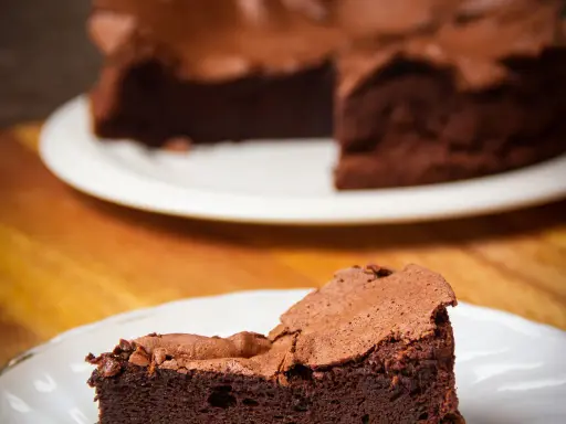 Une part de gâteau au chocolat intense, digne d'un chef pâtissier comme Pierre Hermé, sur une assiette blanche.
